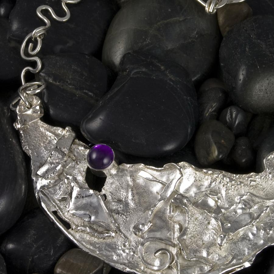 Silver necklace with purple gem on black rocks.