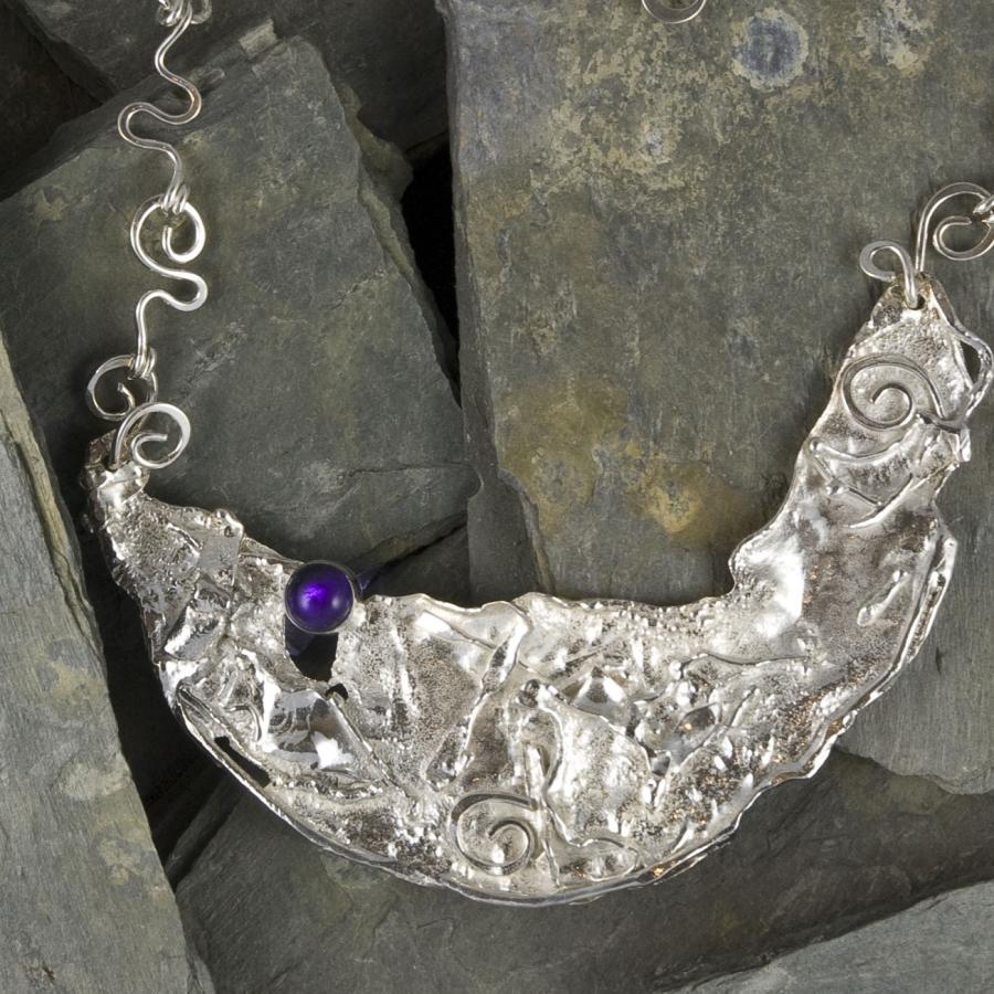 Silver necklace with purple stone on dark slate.