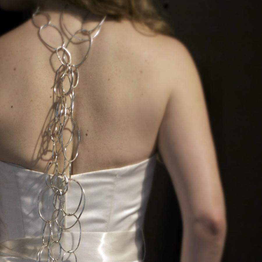 Woman's back in white dress with decorative chain.