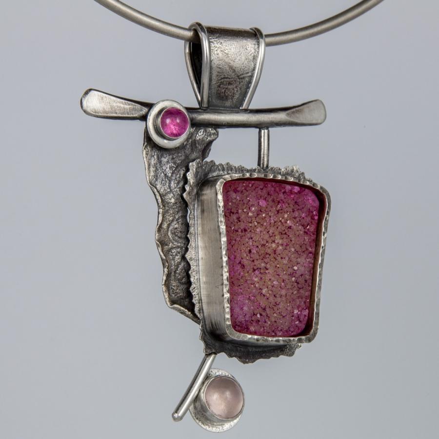 Close-up photograph of silver necklace with pink stone.