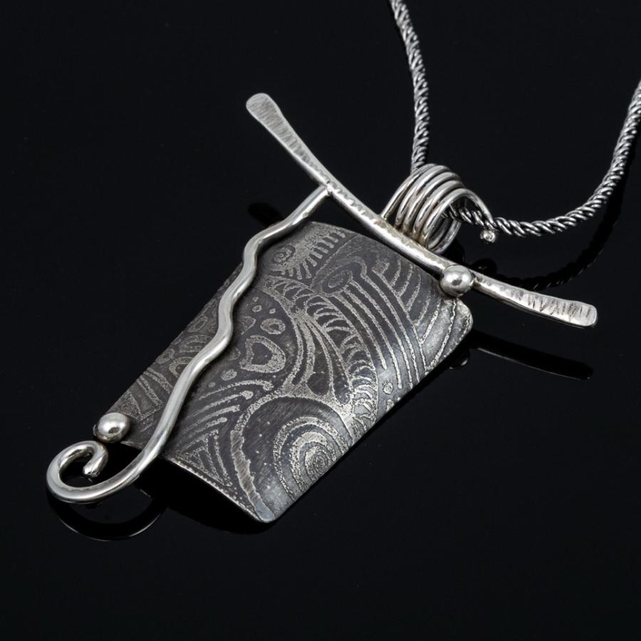 Silver pendant necklace on black background.