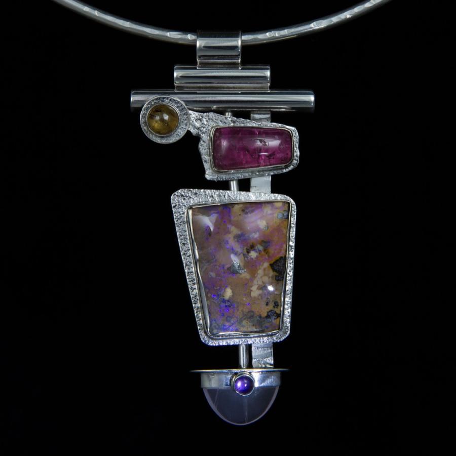 Silver necklace with gem stone pendant on black background.