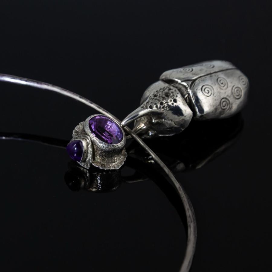 Silver choker necklace with amethyst gem, dark background.