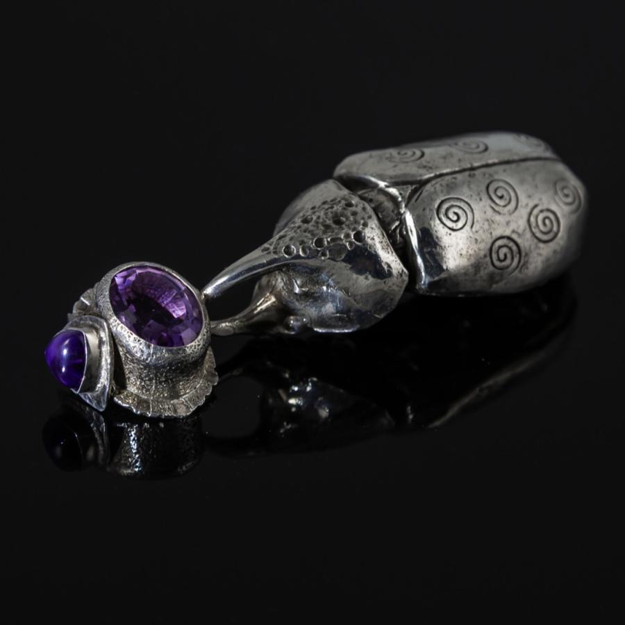 Silver beetle pendant with purple gemstone.