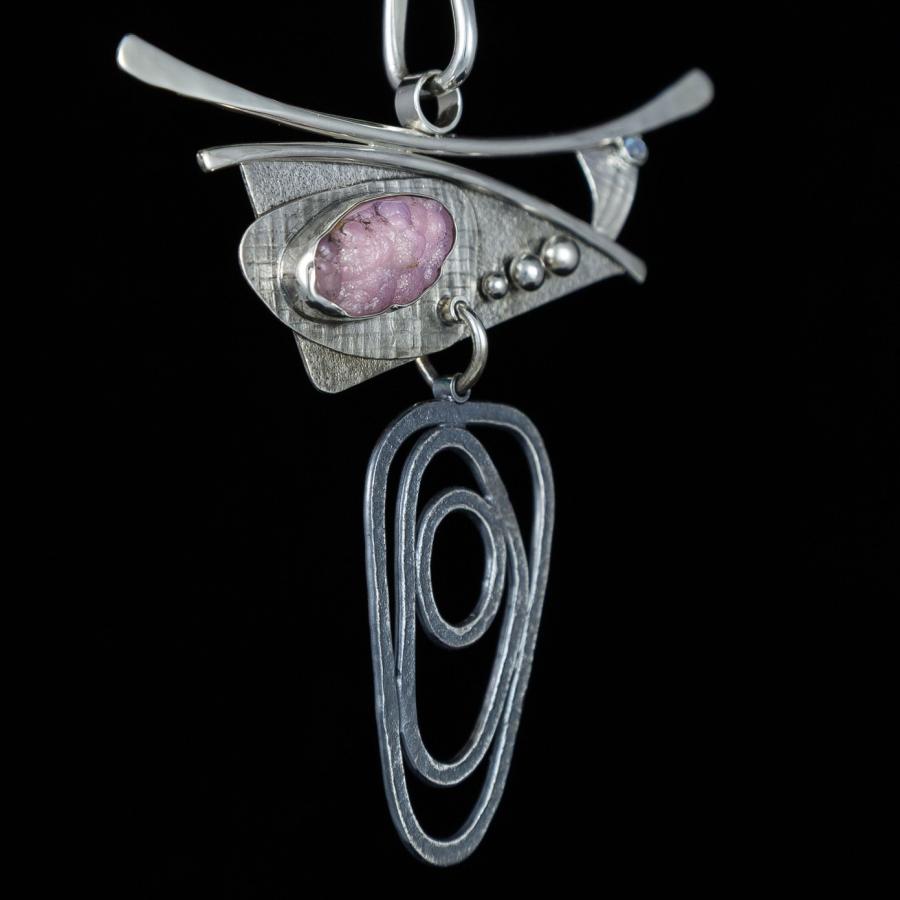 Silver necklace with pink stone on black background.