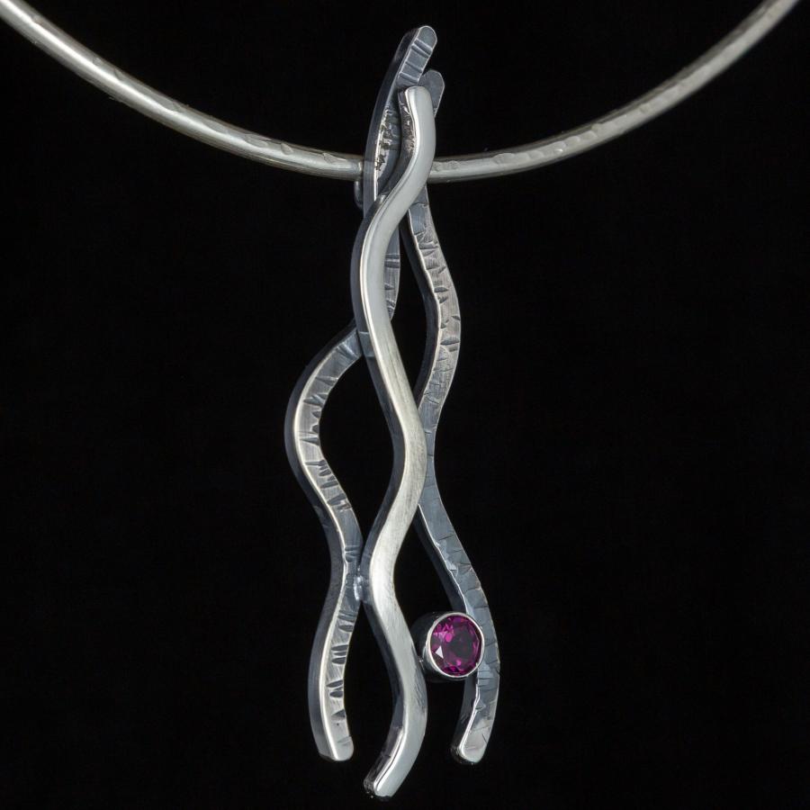 Silver necklace with abstract wave and red stone, close-up.
