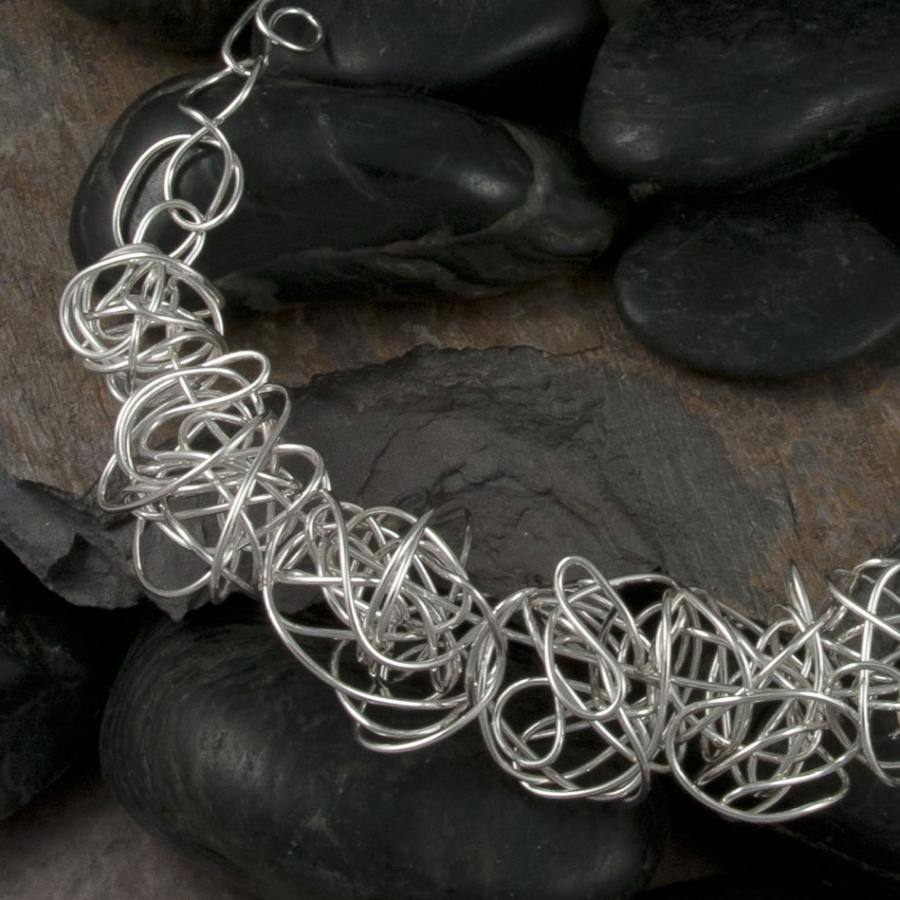 Silver tangled wire necklace on black rocks.