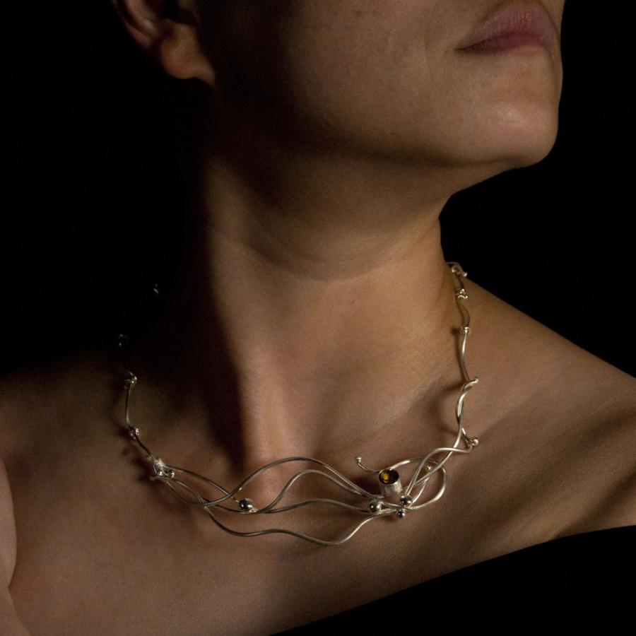 Silver necklace with amber colored gem worn by a model.