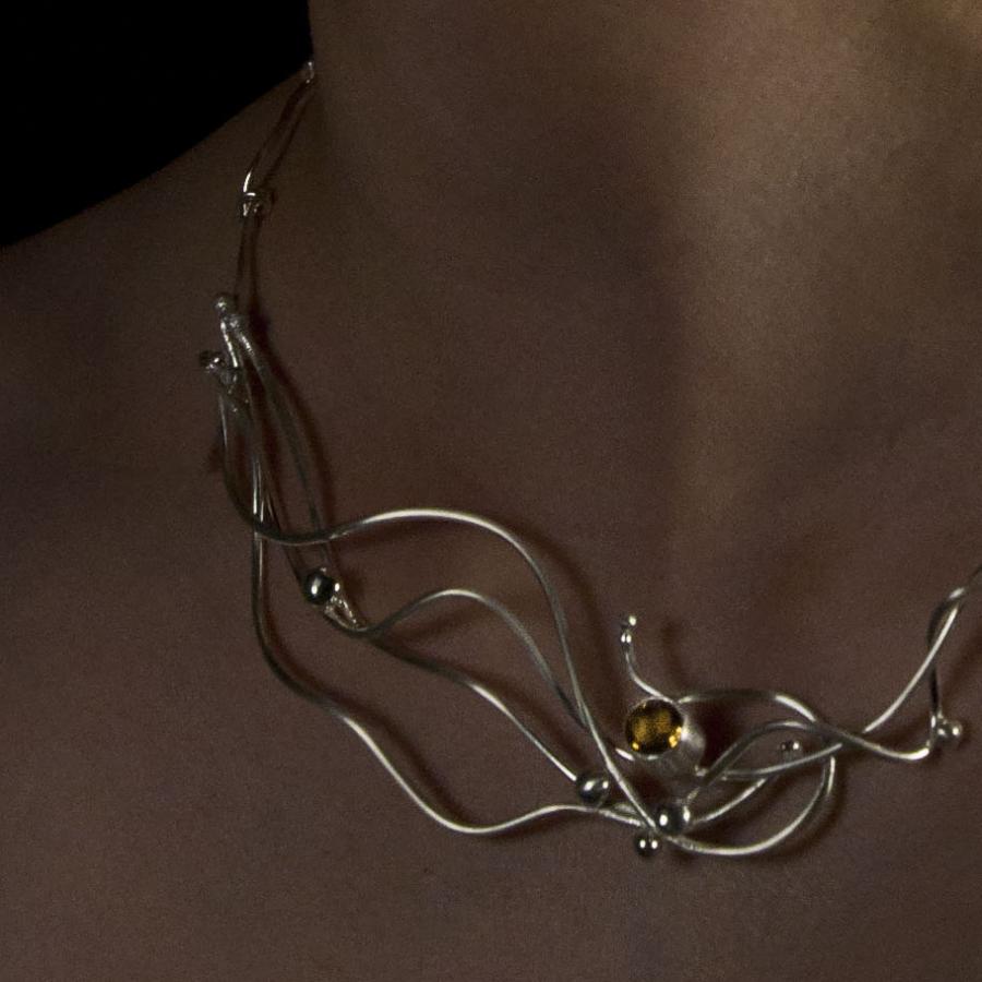 Silver necklace with amber colored gem worn by a model.
