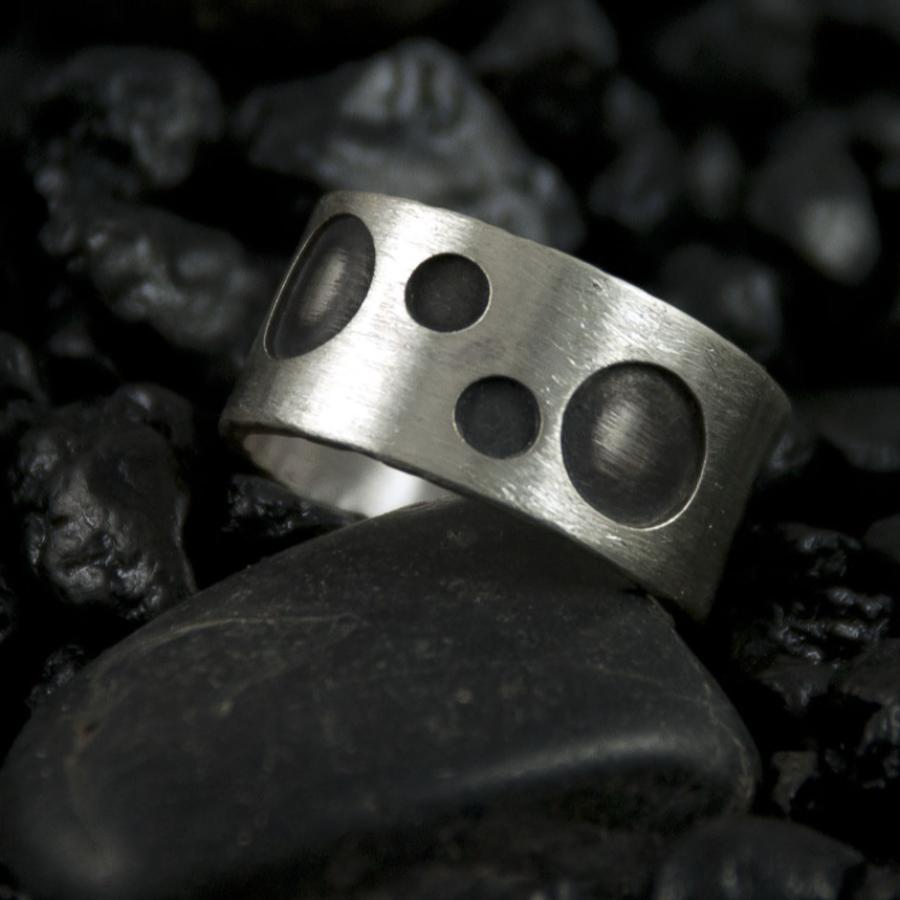 Silver ring with dark circles sitting on black stones.