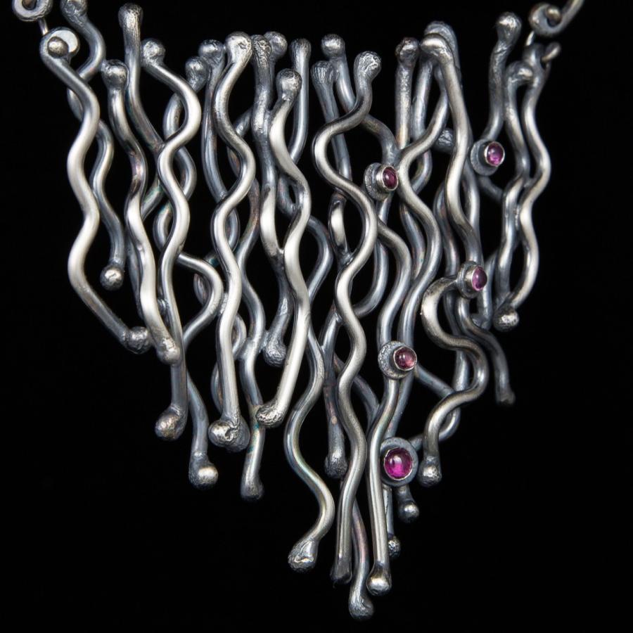 Silver necklace with wavy lines and pink stones.