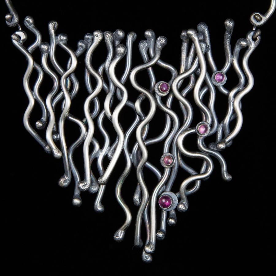 Silver necklace with wavy lines and pink gems.