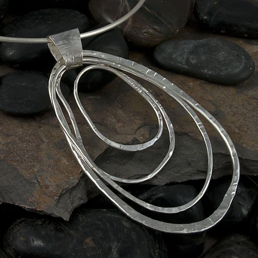 Silver pendant necklace on dark stones, studio photograph.