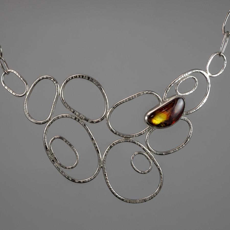 Silver necklace with amber colored stone, photograph.