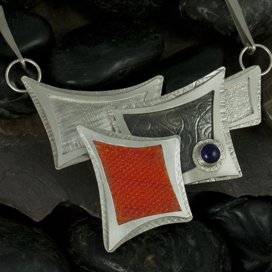 Handcrafted silver necklace on dark rocks, product photograph.