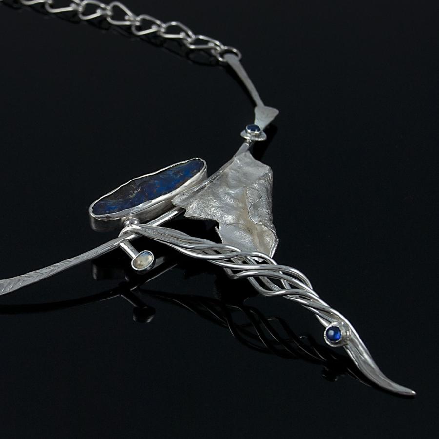 Silver necklace with blue stones on a black surface.