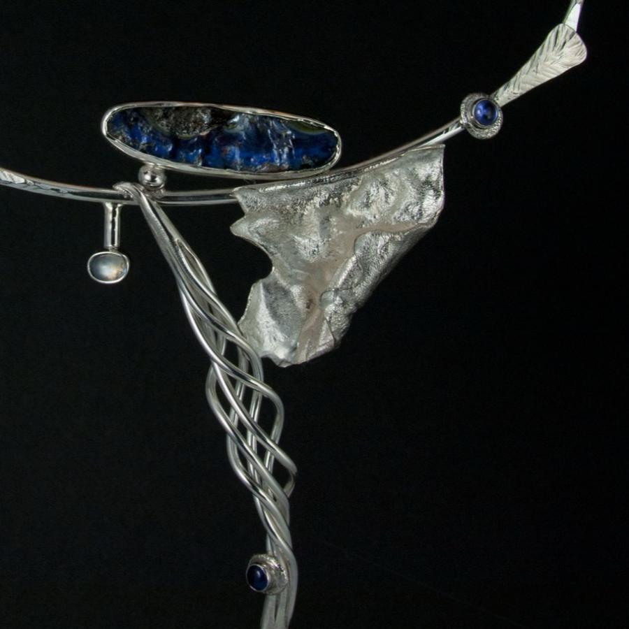 Silver necklace with blue stones on a black surface.