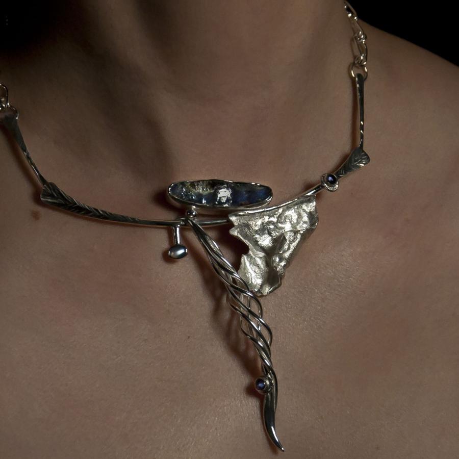 Silver necklace with blue stone worn on bare skin, photograph.