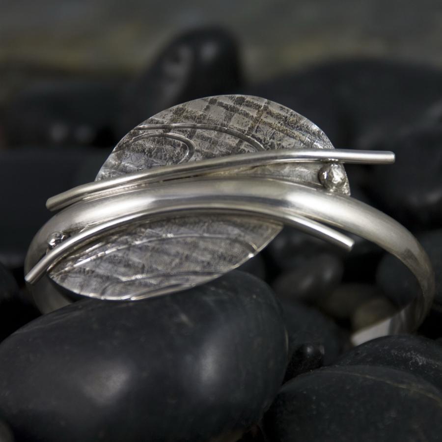Silver bracelet with textured wings on black rocks.