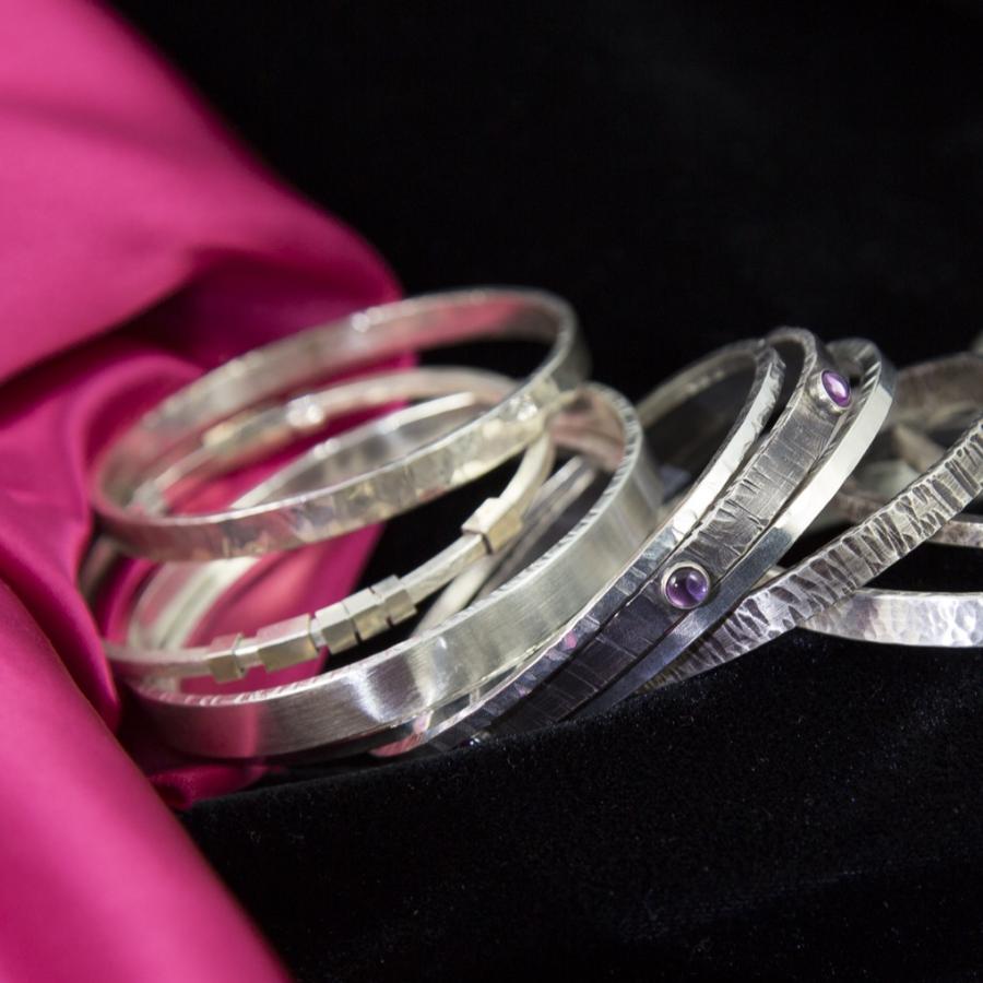 Silver bangle bracelets on pink and black velvet fabric.