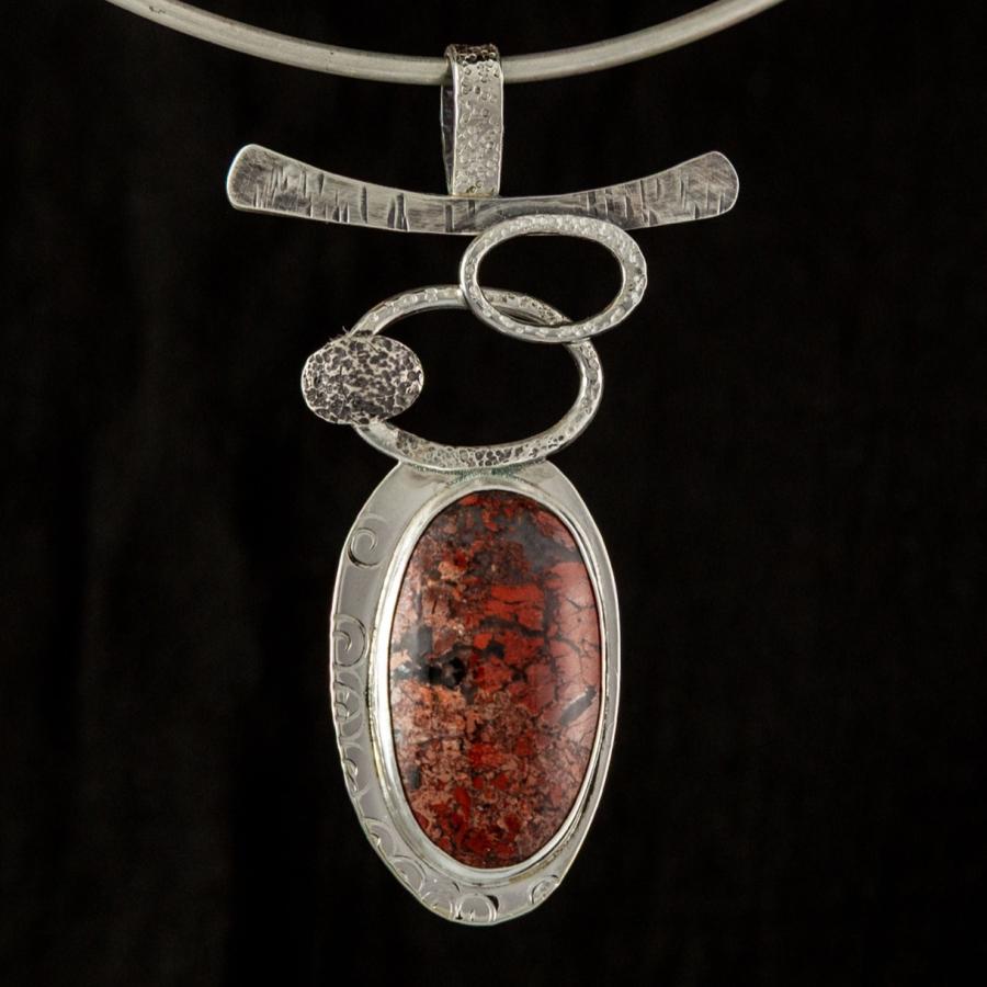Silver pendant with red stone on a black background.