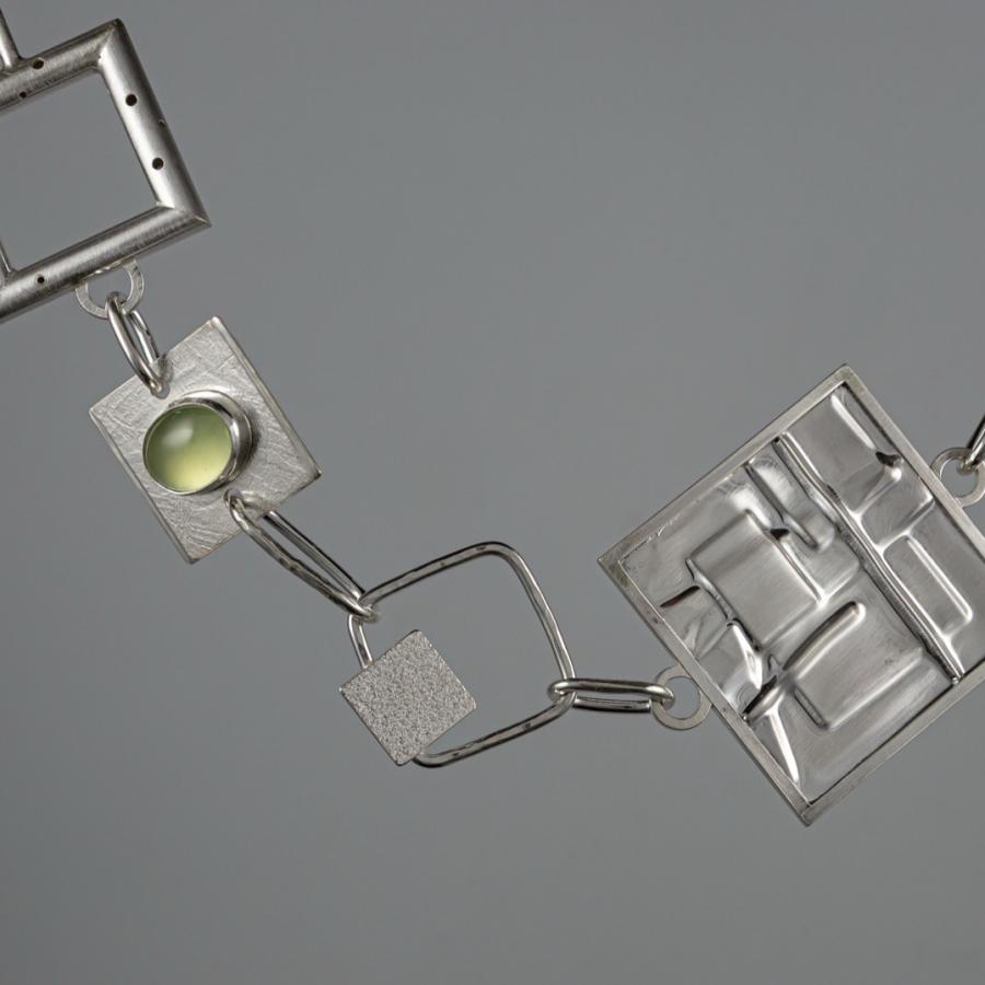 Geometric silver necklace on gray background.