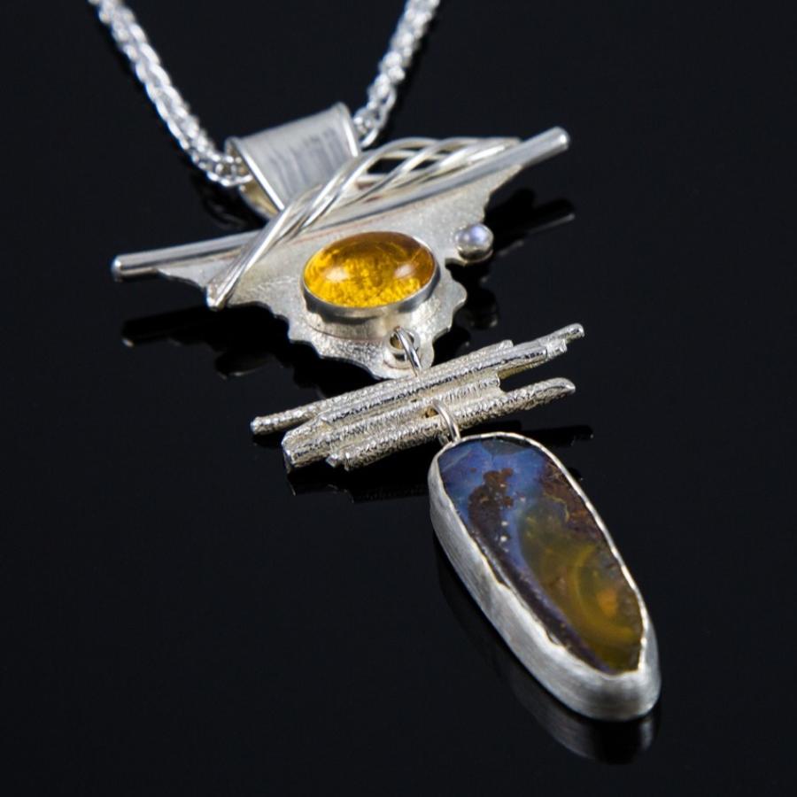 Silver pendant necklace with gold and blue stones on black background.