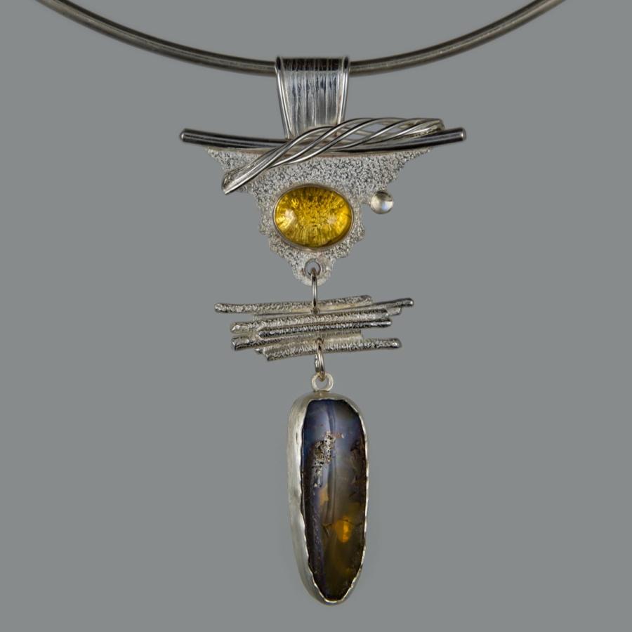 Silver pendant with yellow and dark blue stones, photograph.
