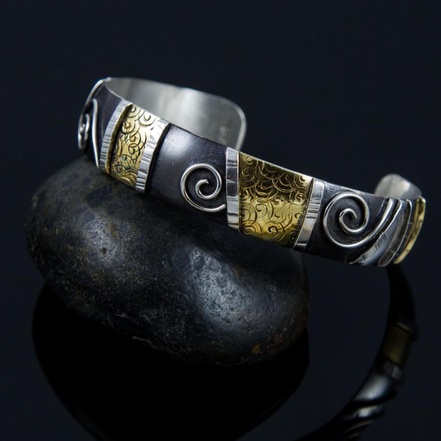 Silver cuff bracelet on a smooth black rock.
