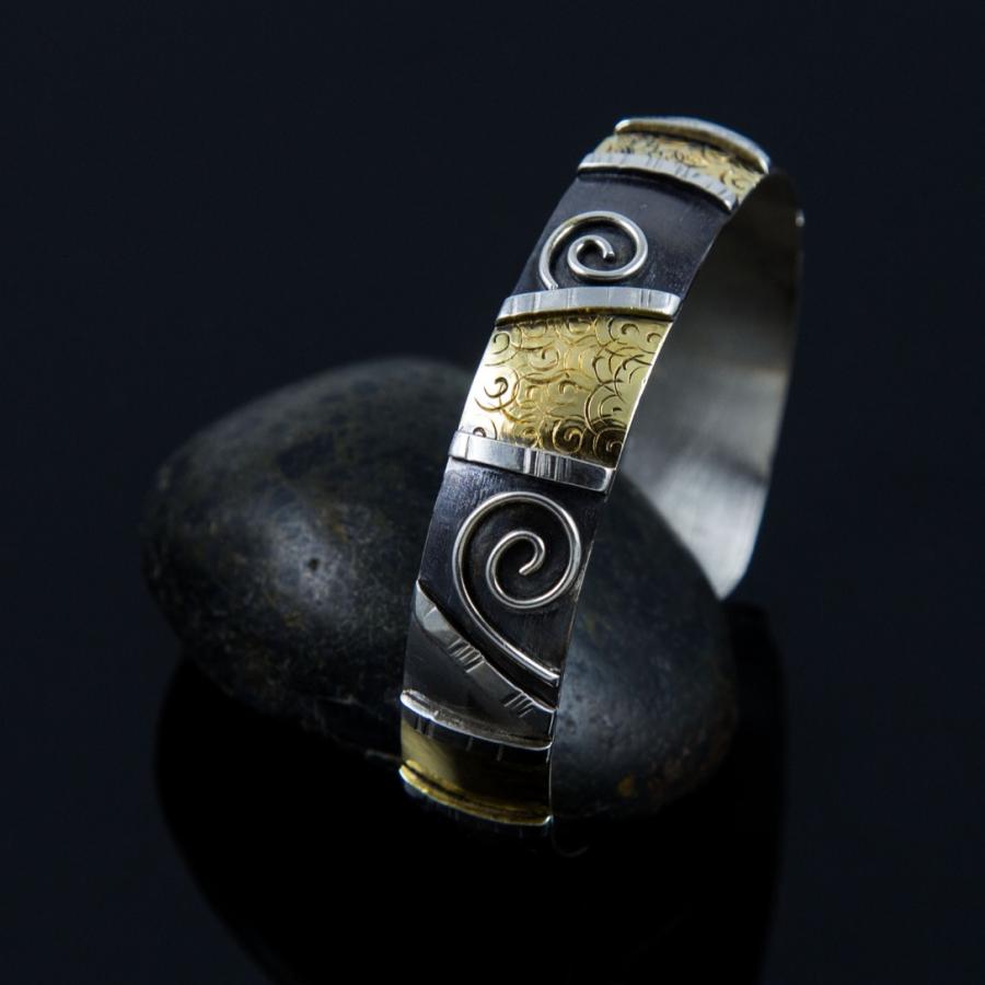 Handcrafted silver and gold cuff bracelet on a dark stone.
