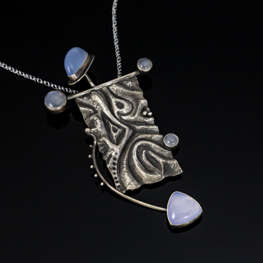 Silver pendant on black background with blue stones