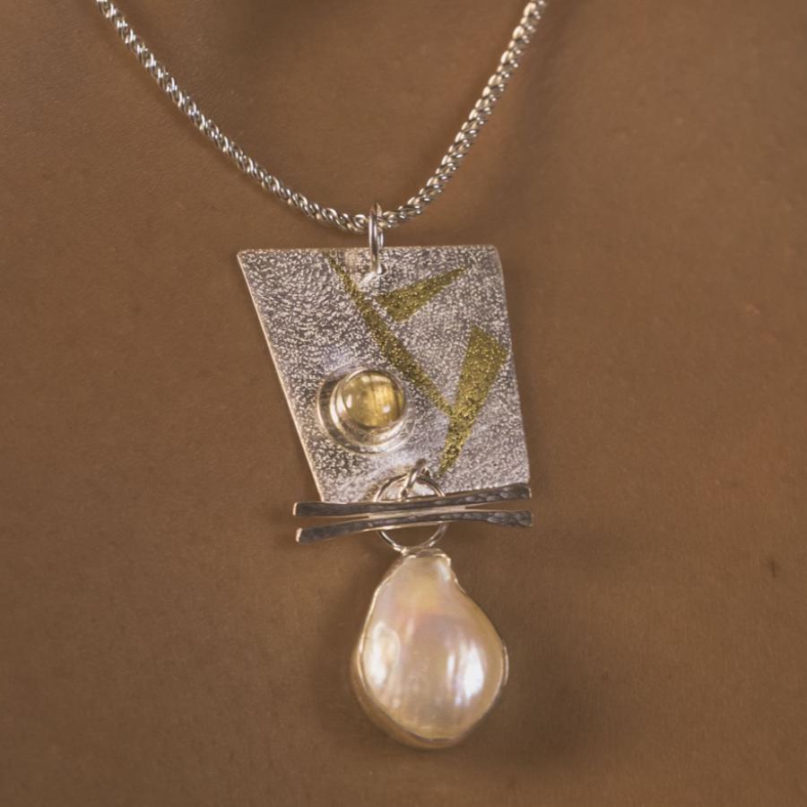 Silver and gold pendant with pearl and rutilated quartz worn by a model