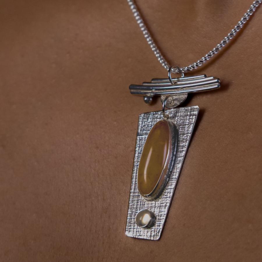 Model wearing a silver pendant with orange and clear stones