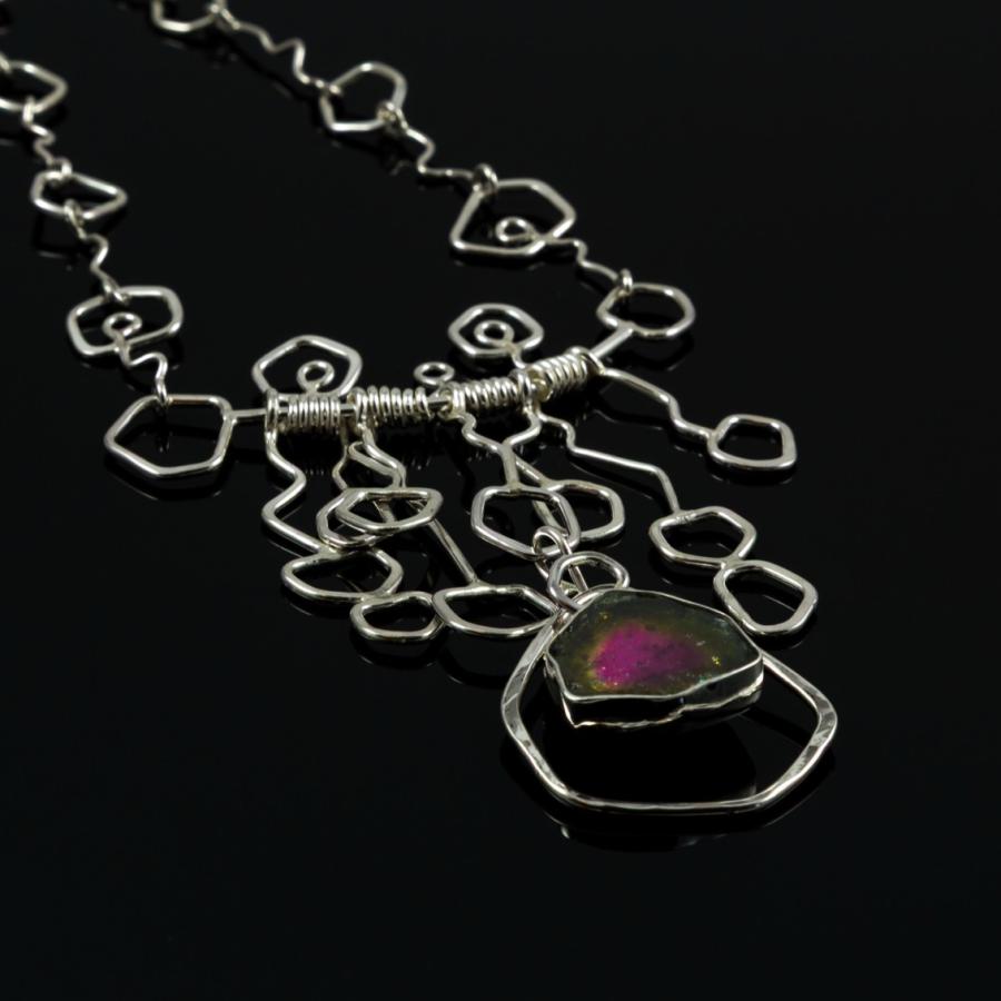 Geometric necklace with repeated 5 sided shapes and a five sided pink and green stone