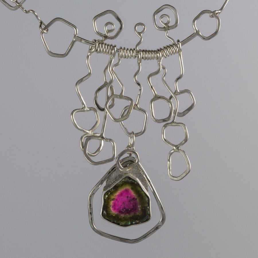 Geometric necklace with repeated 5 sided shapes and a five sided pink and green stone