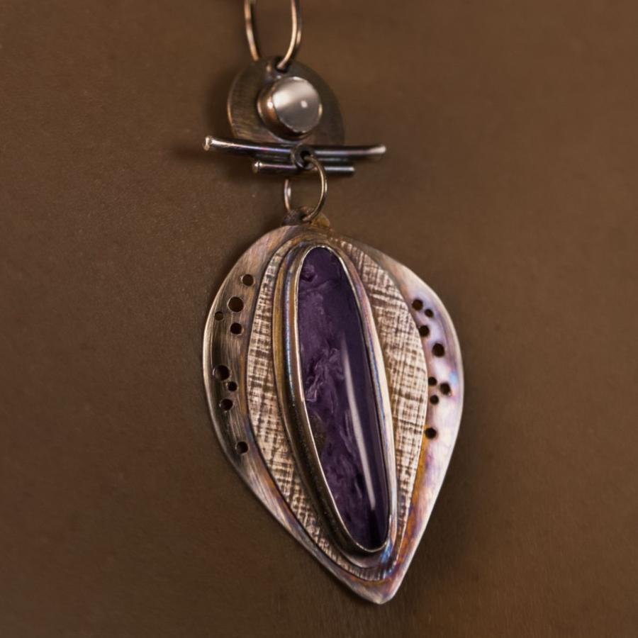 Model wearing a pendant with a prominent purple stone.