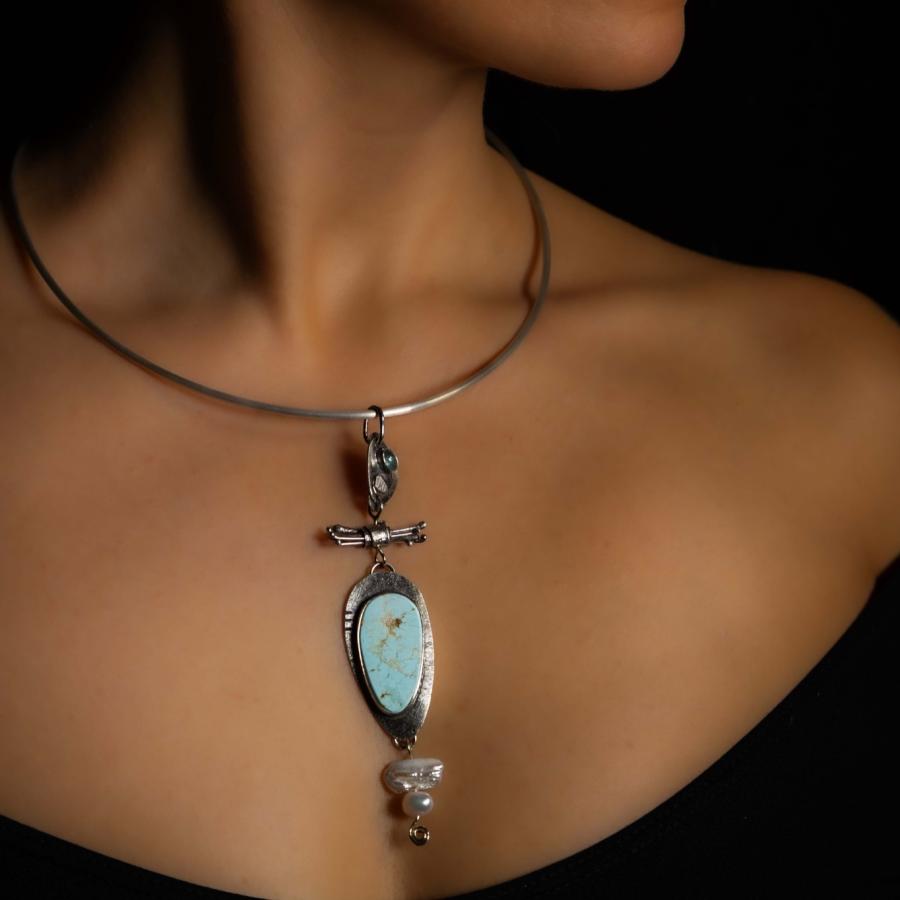 Model wearing a silver pendant with a blue stone and pearls