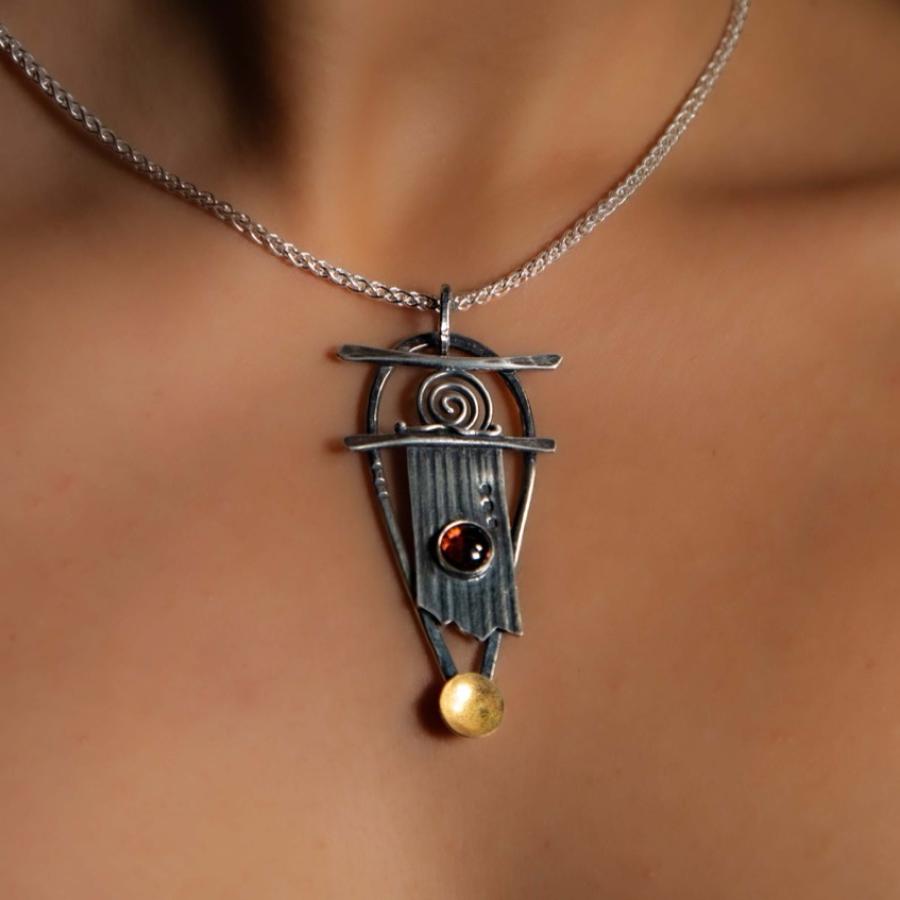 Model wearing a silver pendant with a red stone and gold accents.