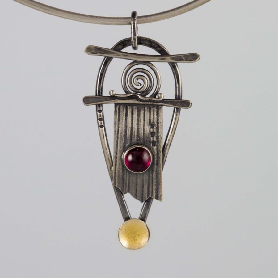 A silver pendant with a red stone and gold accents.