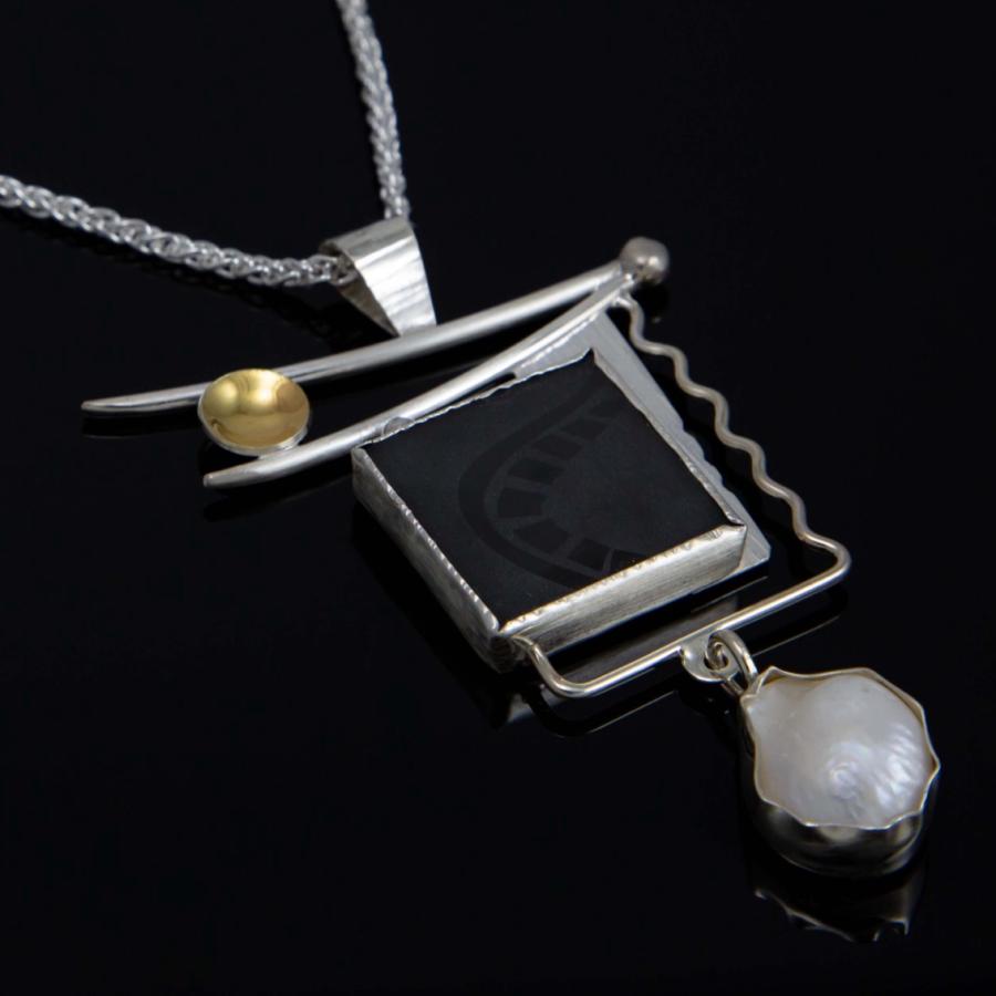 A silver pendant with an etched black stone, pearl, and gold accent.