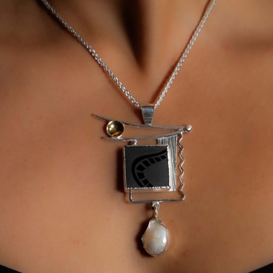 A model wearing a silver pendant with an etched black stone, pearl, and gold accent.