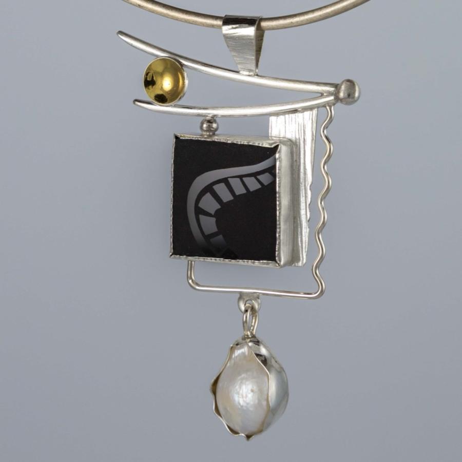 A silver pendant with an etched black stone, pearl, and gold accent.