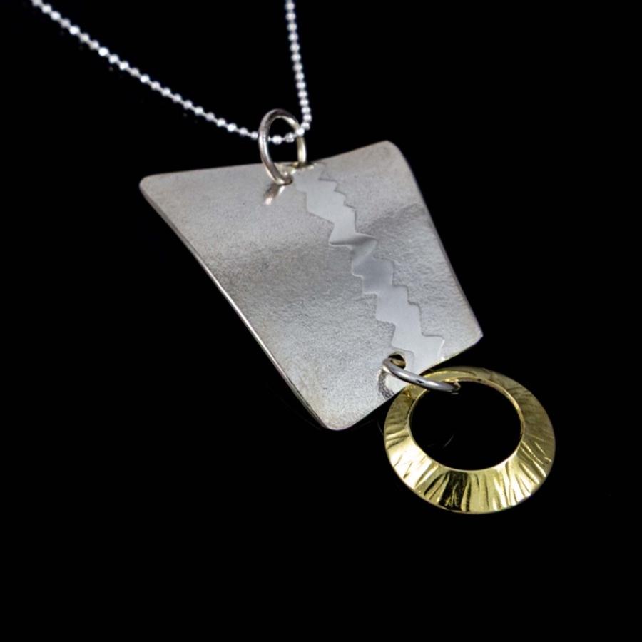 Photograph of a geometric silver pendant with a small gold-toned ring, hanging on a thin chain.