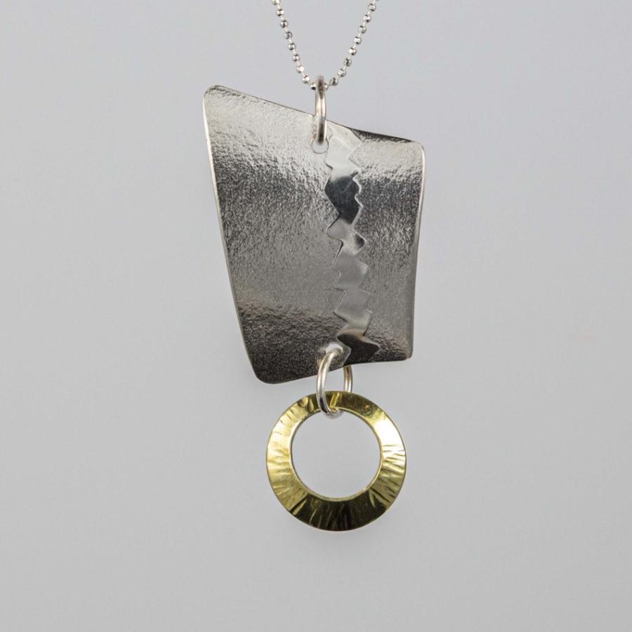 Photograph of a geometric silver pendant with a small gold-toned ring, hanging on a thin chain.