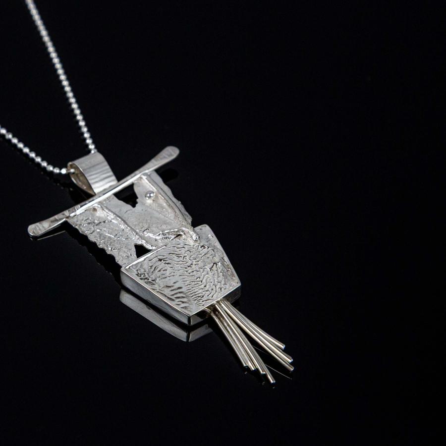Photograph of a textured silver pendant on a delicate chain against a black background.