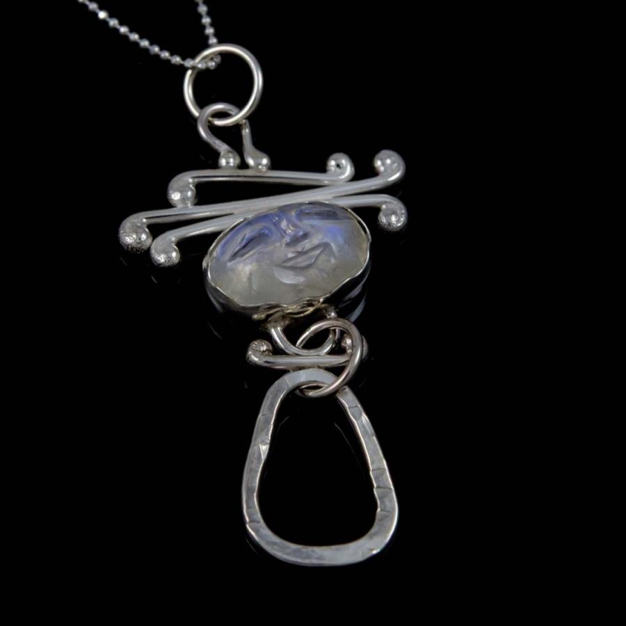 Photograph of a silver pendant with a central moonstone on a chain against a black background.