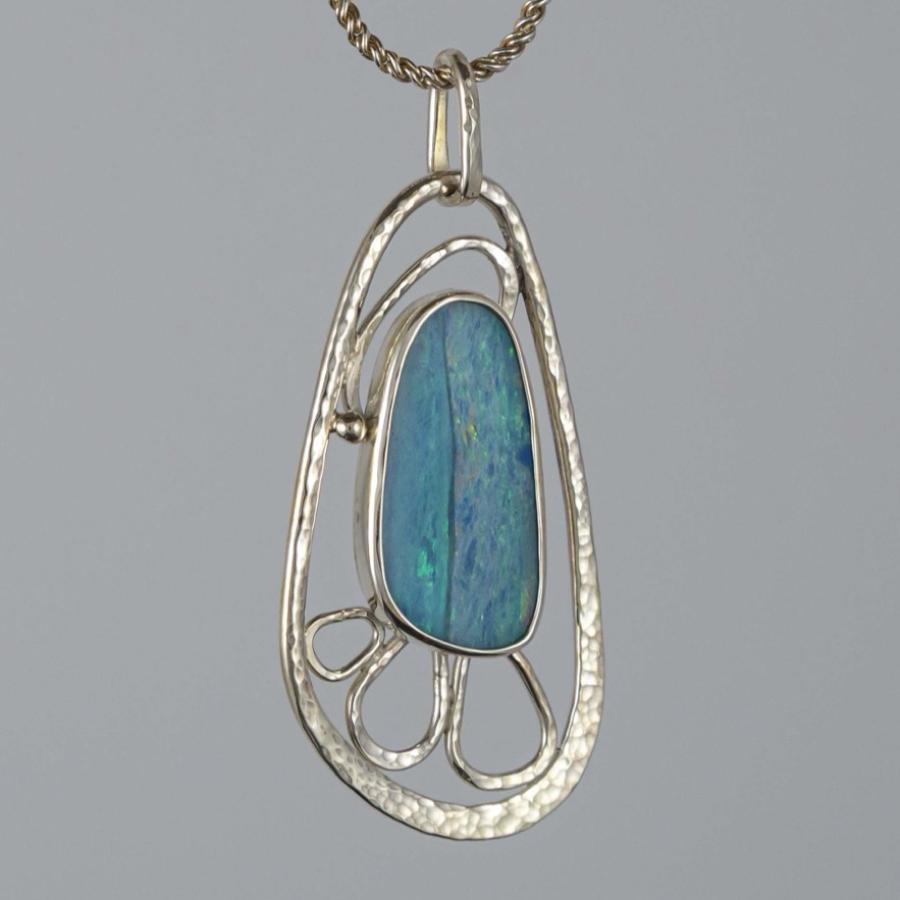 Photograph of an oval blue opal pendant set in a textured silver frame on a chain.