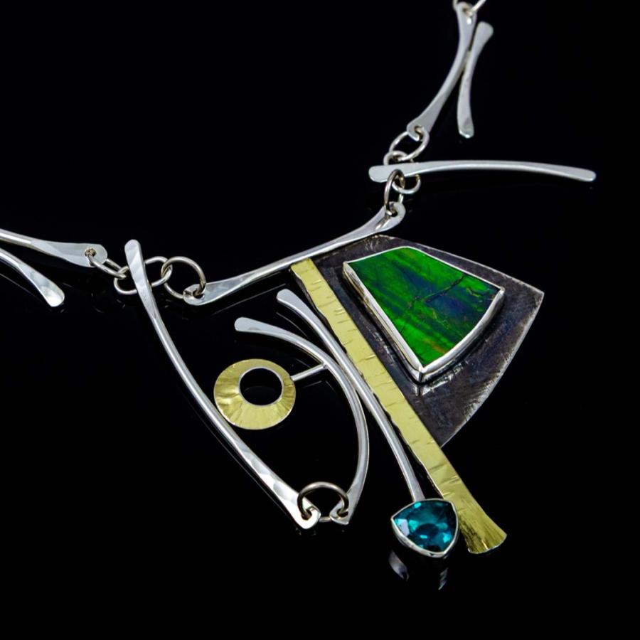 Photograph of a modern silver necklace featuring a green stone and geometric gold accents.