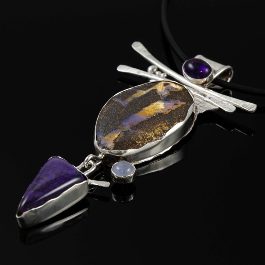 Photograph of a silver pendant featuring an oval stone, a triangular purple gem, and an amethyst.