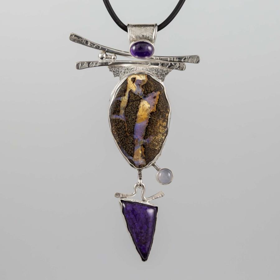 Photograph of a silver pendant featuring an oval stone, a triangular purple gem, and an amethyst.